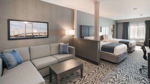 Habitación de hotel con sofá, dos camas, escritorio y un amplio ventanal con cortinas.