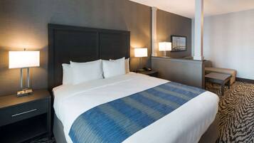 Una habitación de hotel con una cama grande, dos mesitas de noche con lámparas, un escritorio pequeño y una silla.