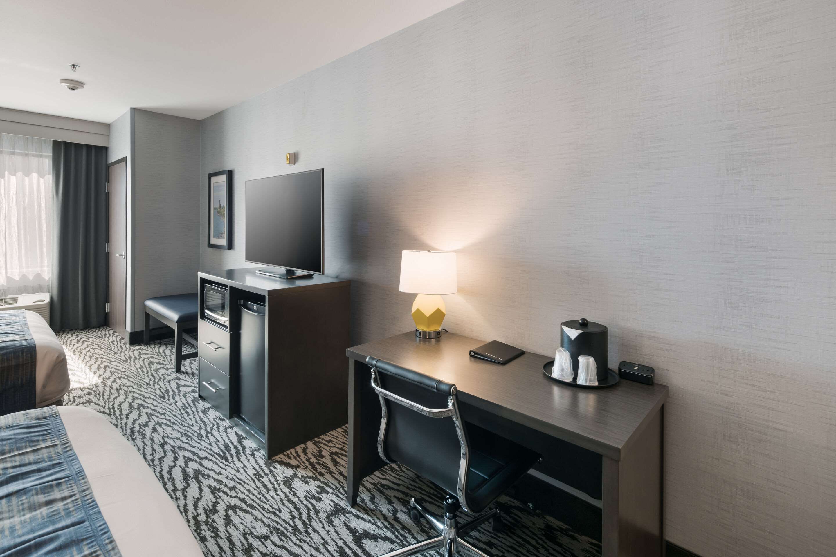 A hotel room with a bed, a desk with a lamp, a television, and a coffee maker.