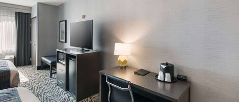 A hotel room with a bed, a desk with a lamp, a television, and a coffee maker.
