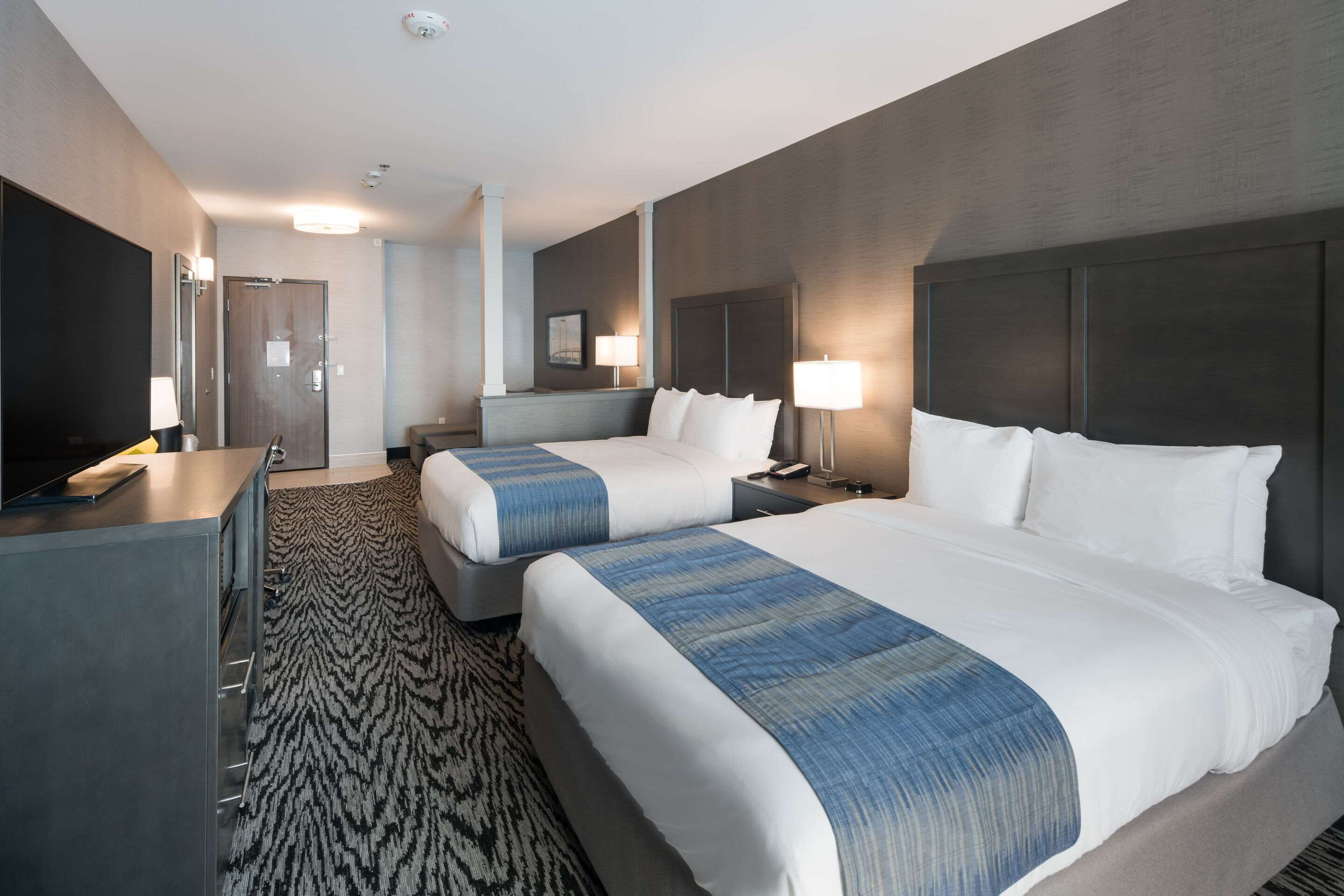 A hotel room with two beds, a desk, a television, and a patterned carpet.