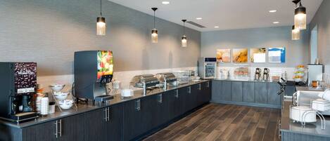 A modern kitchen with a long counter, overhead pendant lights, and a coffee station.