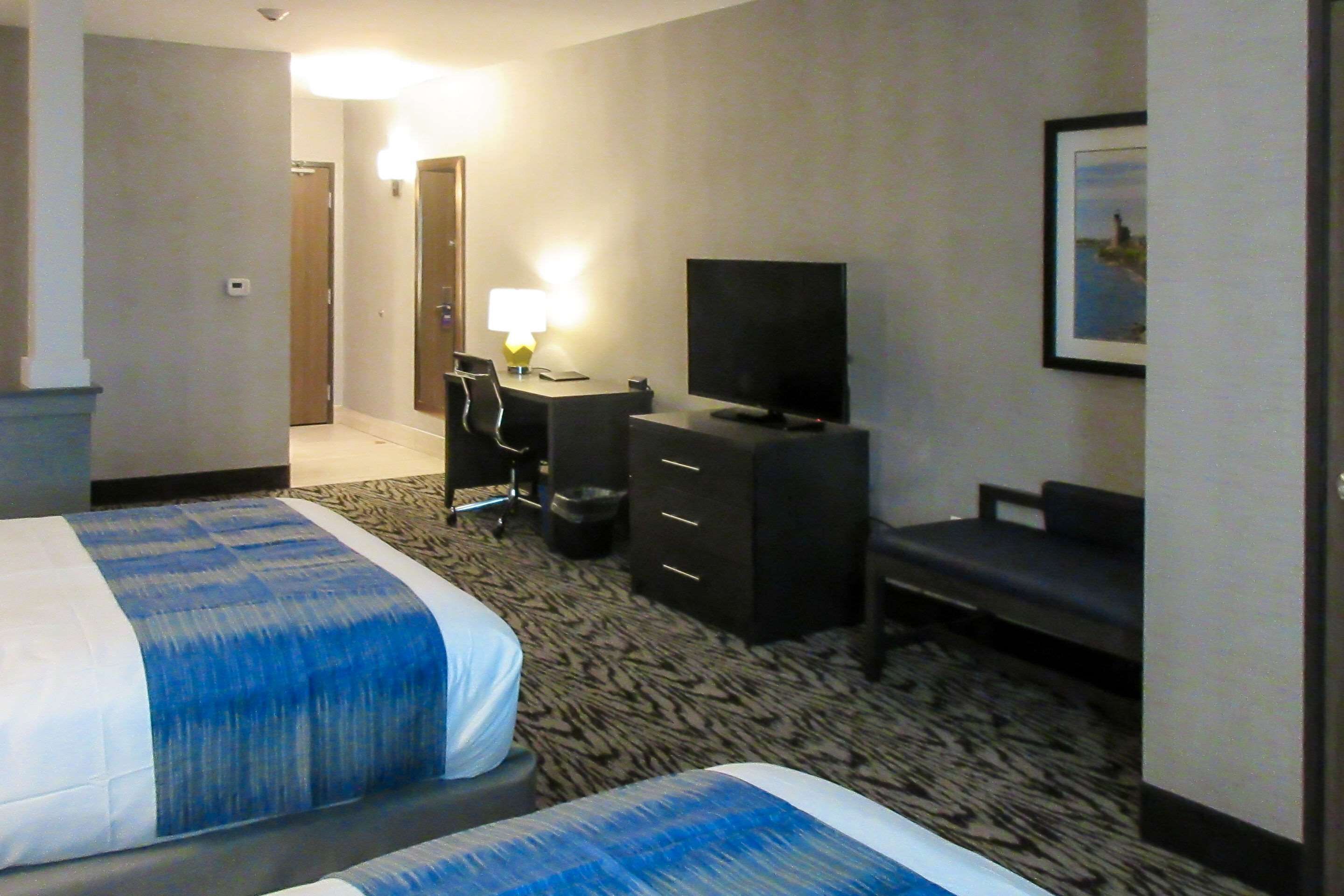 A hotel room with two beds, a desk with a chair, a television, and a framed picture on the wall.