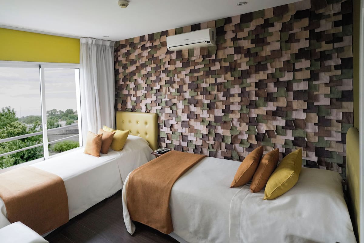 Une chambre d’hôtel avec deux lits, une grande fenêtre et un mur décoré de motifs.