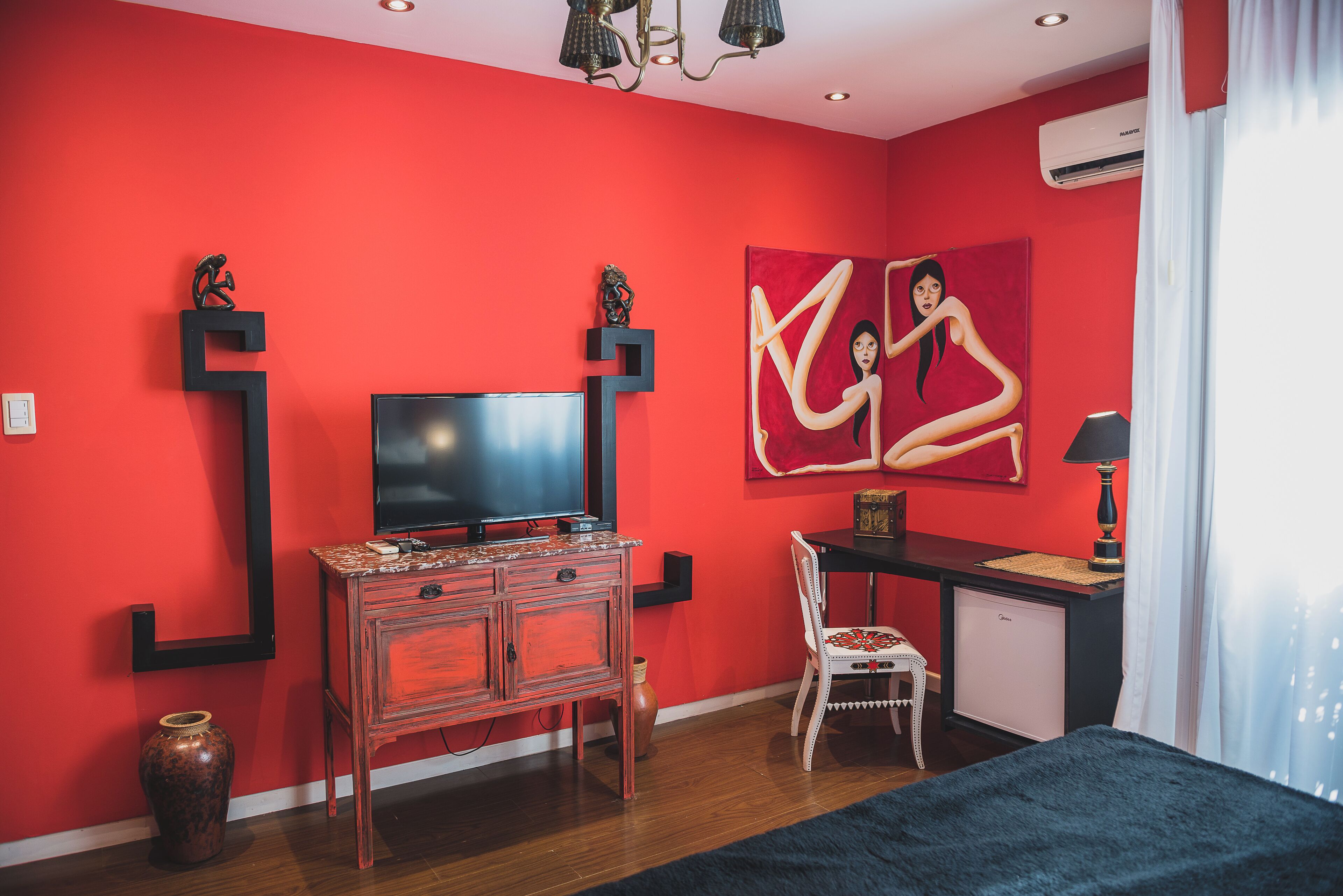 Een kamer met een rode wand, een flatscreen televisie, een bureau, een stoel en een bed.