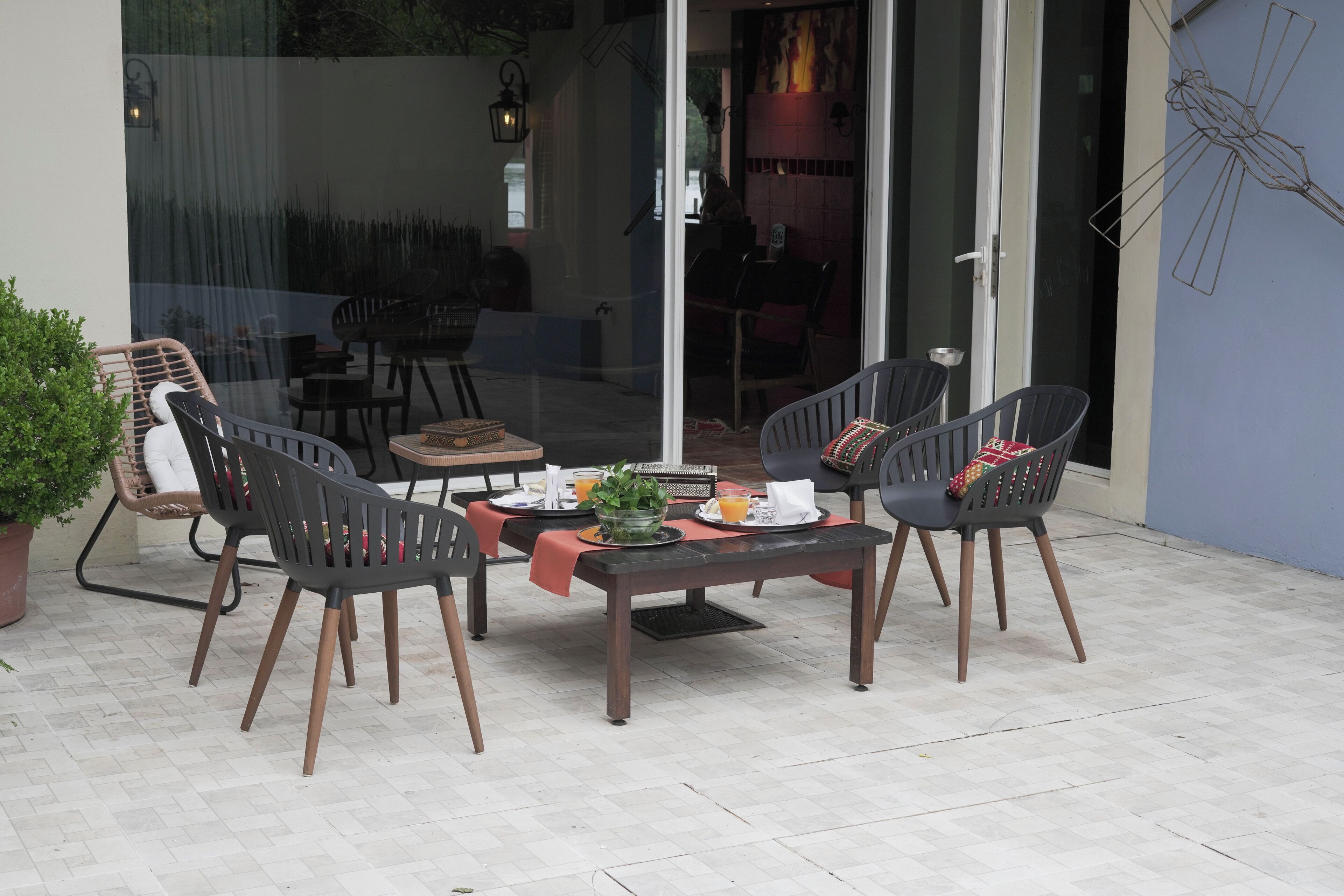 En udendørs terrasse med et bord dækket til to personer, omgivet af fire stole og en potteplante ved siden af.