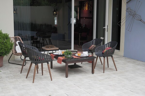 Un patio al aire libre con una mesa preparada para dos personas, rodeada de cuatro sillas y una planta en maceta al lado.