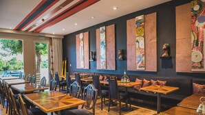 A restaurant with wooden tables and chairs, a black sofa, and colorful artwork on the walls. - Hotel Boutique Los Muelles (Carmelo)