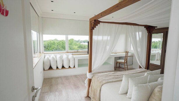 A bedroom with a four-poster bed, a desk with a chair, and a view of greenery through large windows. - Hotel Boutique Los Muelles (Carmelo)