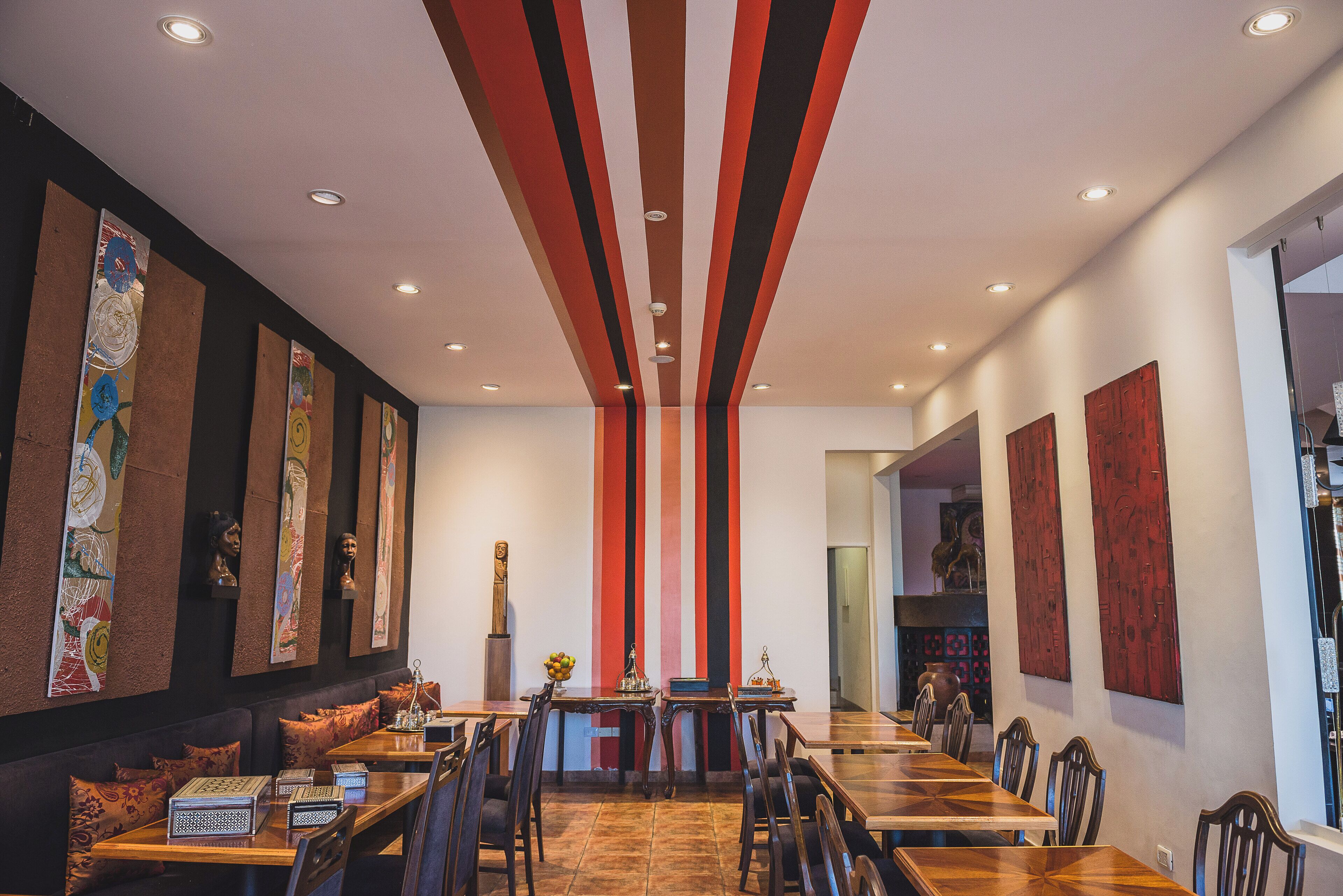 A modern dining area with long tables and chairs, a central decorative column, and artwork on the walls.