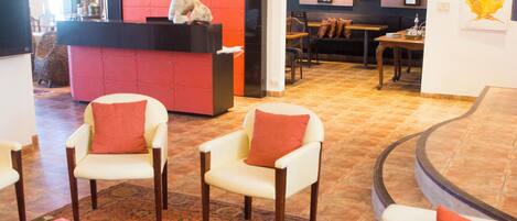 Un amplio salón con sofá, sillones y una mesa de centro. Se ve un mostrador de recepción al fondo.