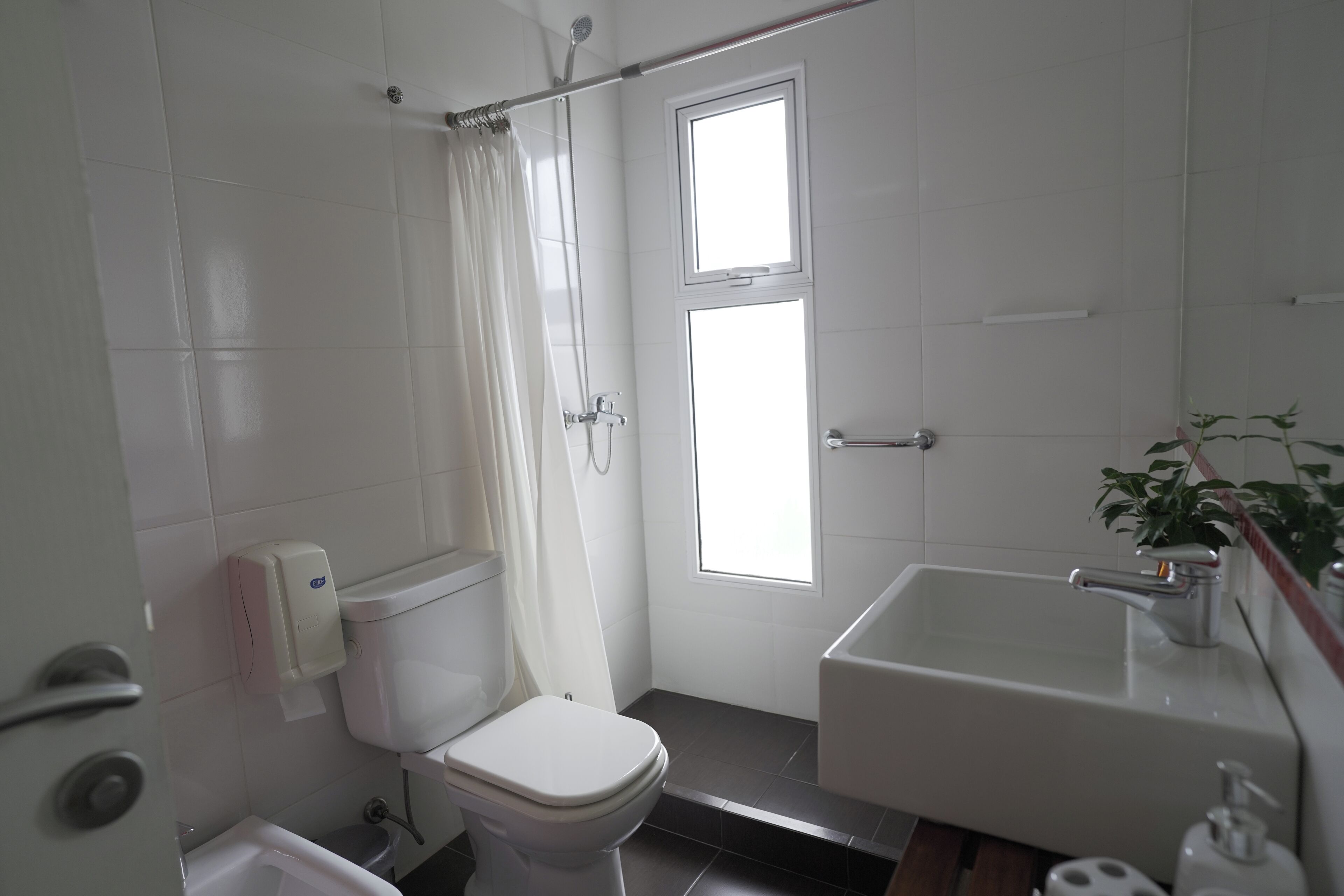 A bathroom with a toilet, shower, sink, and a window providing natural light.