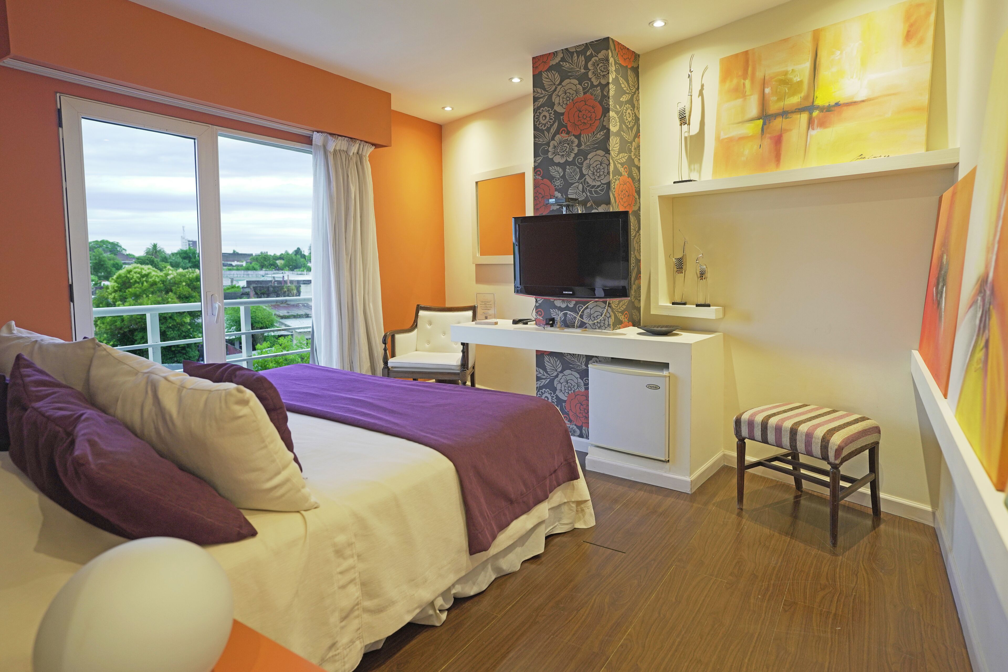 Habitación de hotel con cama, escritorio, televisor y vistas a zonas verdes.