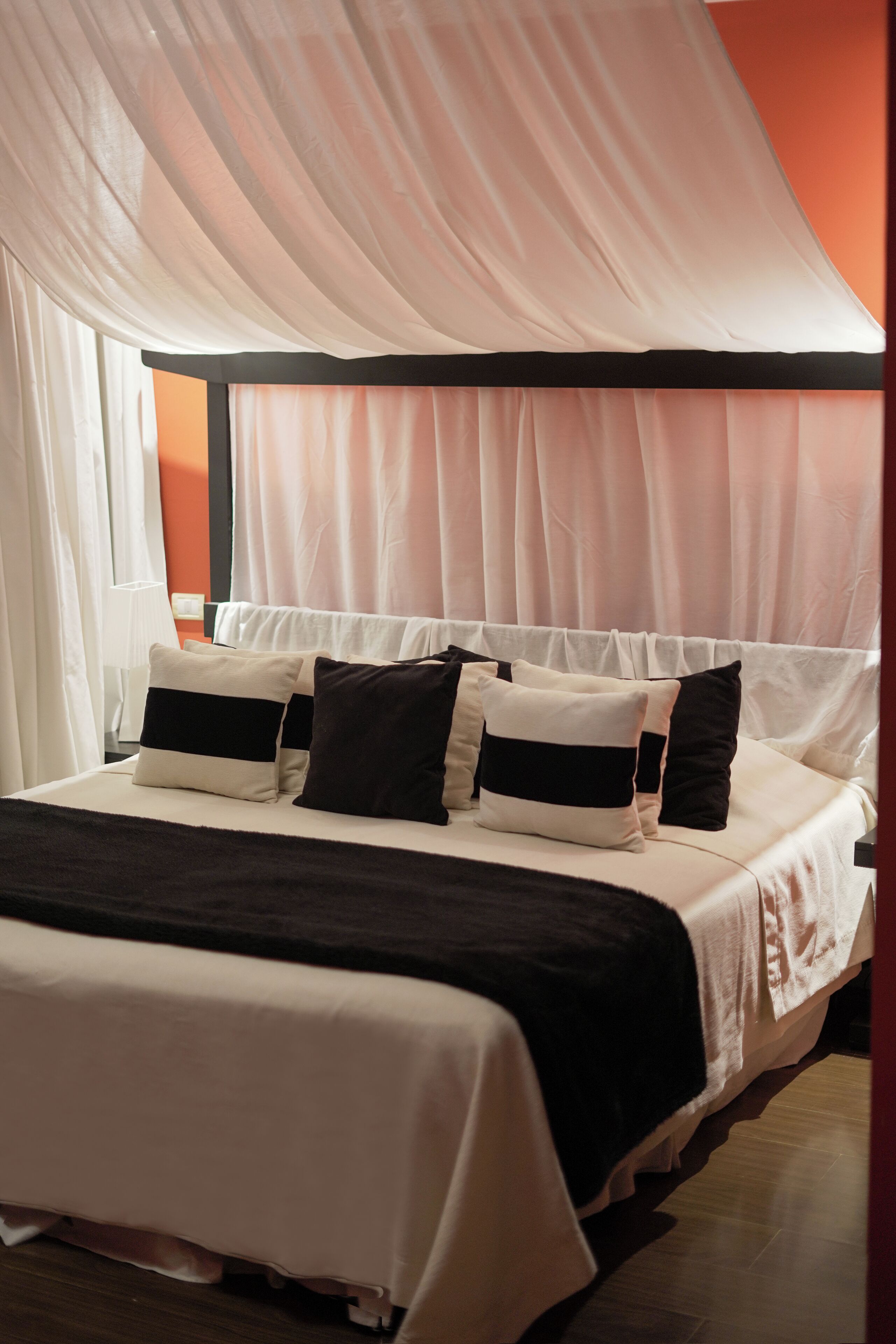 A neatly made bed with a black and white bedspread, white and black pillows, and sheer white curtains.