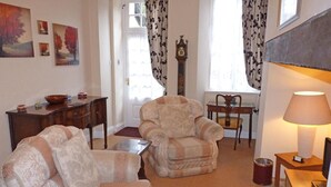 A living room with a sofa, armchair, and a small table. There is a clock on the wall and a lamp on a side table. - Town Mills B &B (Dulverton)