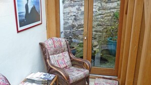 A sunroom with wicker furniture, a stone wall, and a framed picture. - Town Mills B &B (Dulverton)