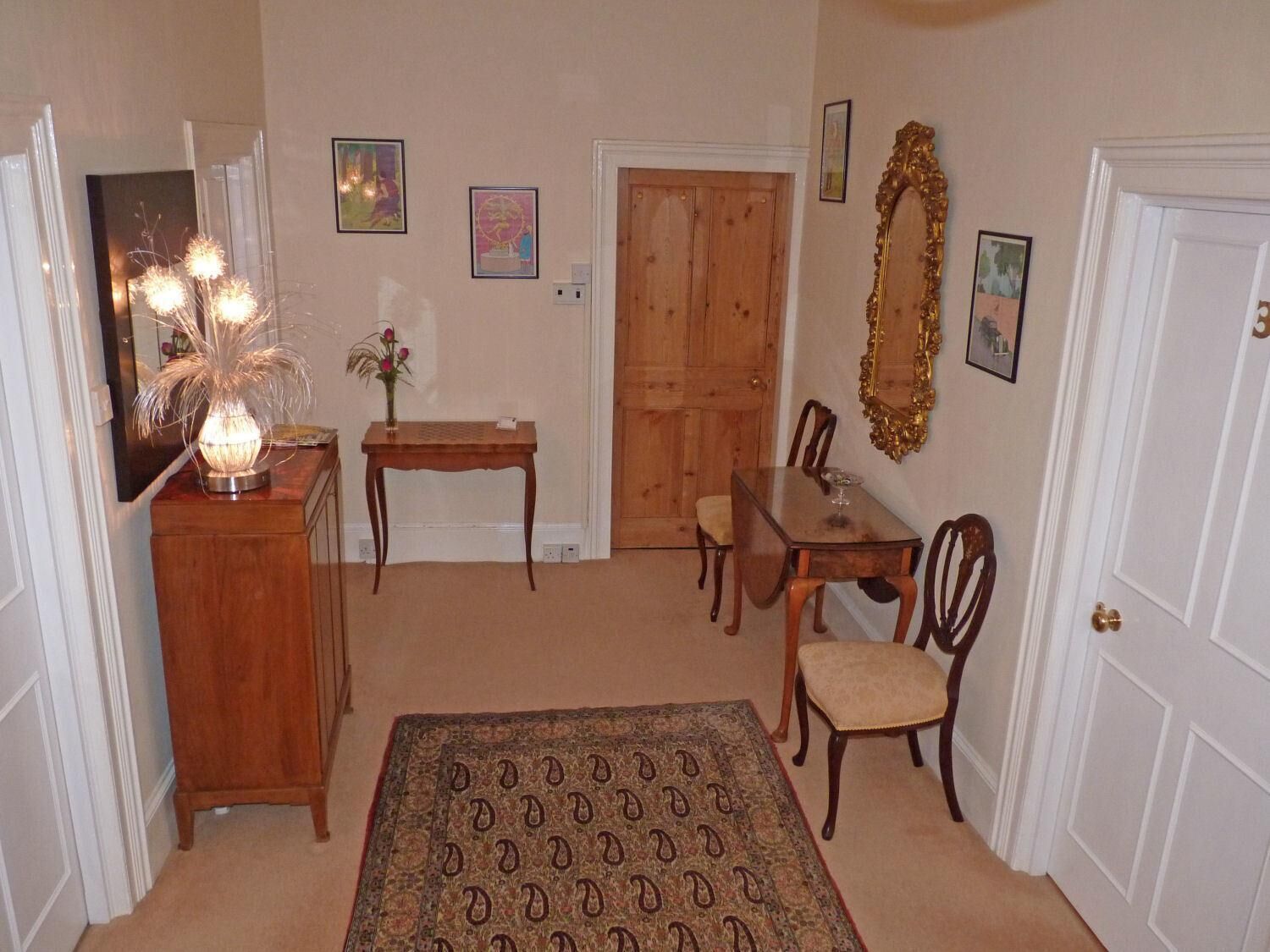 A hallway with a dining area, wooden furniture, a patterned rug, and wall-mounted artwork.