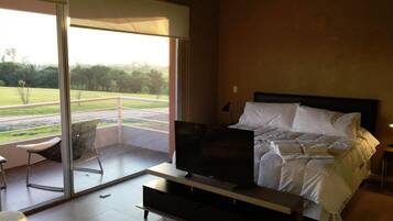 Un dormitorio con cama, televisión y balcón con una silla.