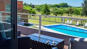 Ein Balkon mit Korbmöbeln, ein Pool und Blick auf eine grüne Landschaft.