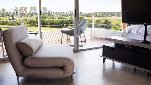 Ein modernes Zimmer mit einer Couch, einem Fernseher und einem Balkon mit Blick auf Grünflächen und ein Gebäude.