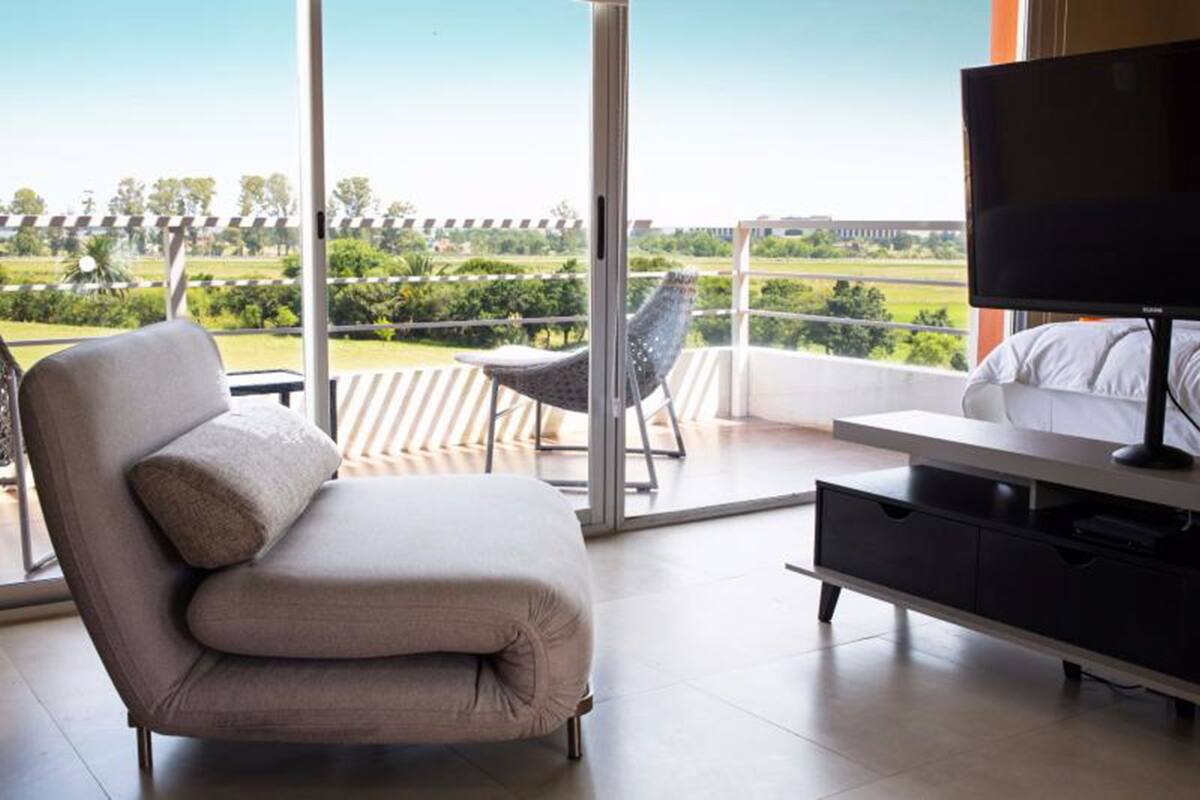 A modern room with a sofa, a TV, and a balcony with a view of greenery and a building.