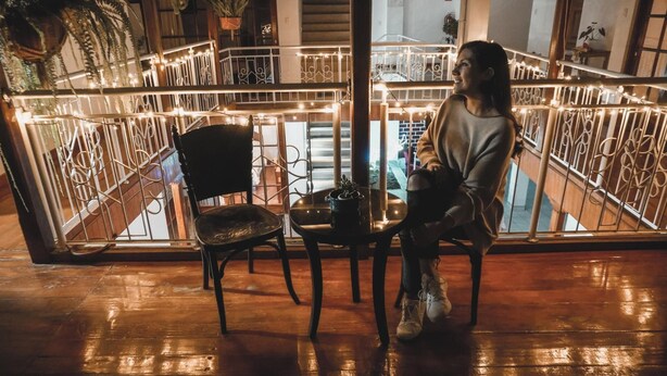 A person sitting on a chair by a railing with string lights, overlooking a staircase and a balcony. - Casa Kuelap Hostal (Chachapoyas)