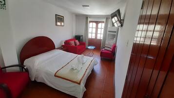 Una habitación de hotel con una cama, un sofá rojo, una mesita y un televisor instalado en la pared.