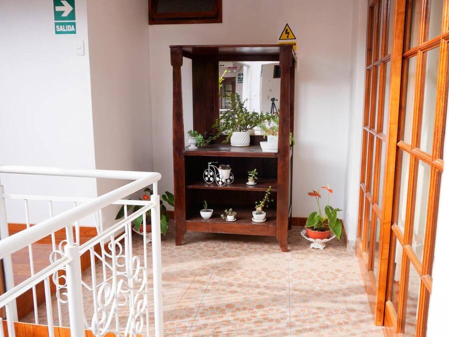 A hallway with a wooden shelf holding potted plants, a white railing, and a tiled floor.