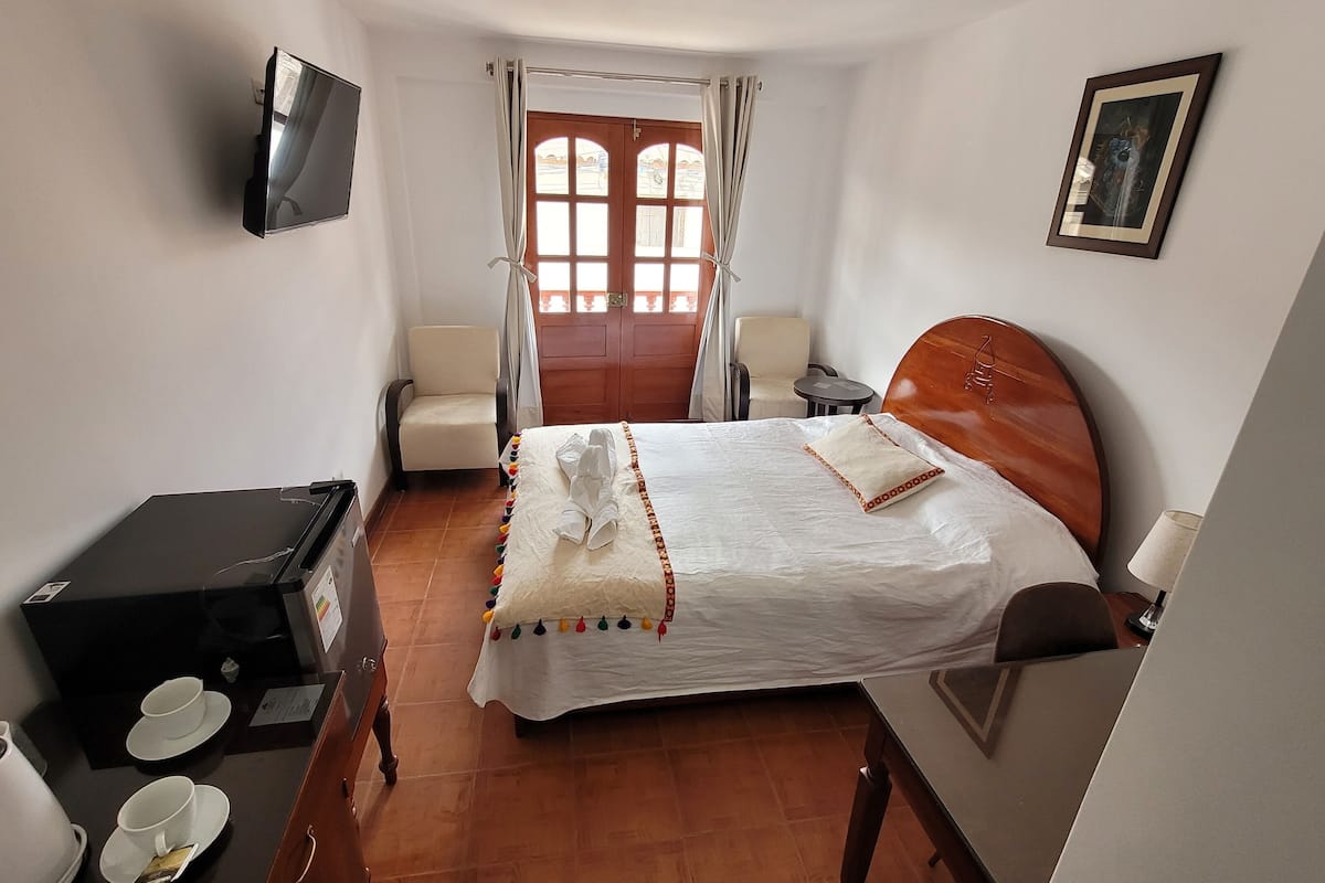 A hotel room with a bed, a desk, a chair, a TV, and a window with curtains.
