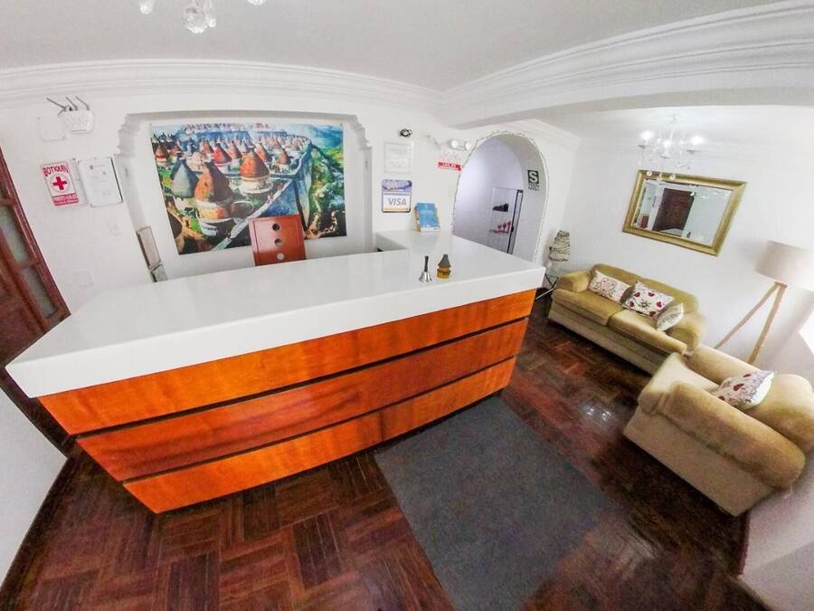 Un mostrador de recepción con una superficie blanca y cajones de madera, un cuadro encima y un sofá con cojines al fondo.