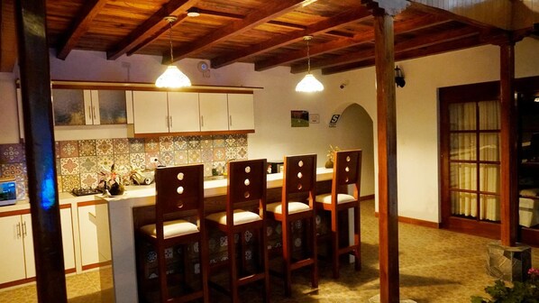 A kitchen with wooden cabinets, a tiled backsplash, and a bar area with four chairs. - Casa Kuelap Hostal (Chachapoyas)