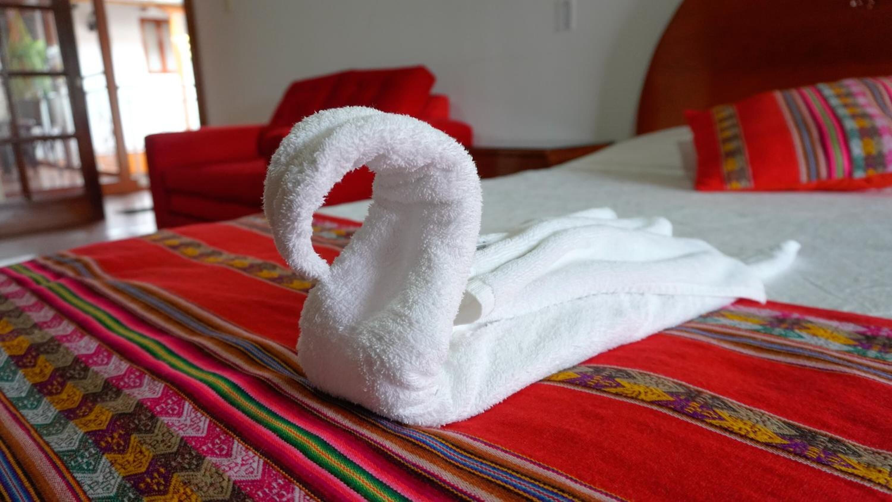 A bed with a white swan towel, a red blanket, and a colorful patterned blanket.