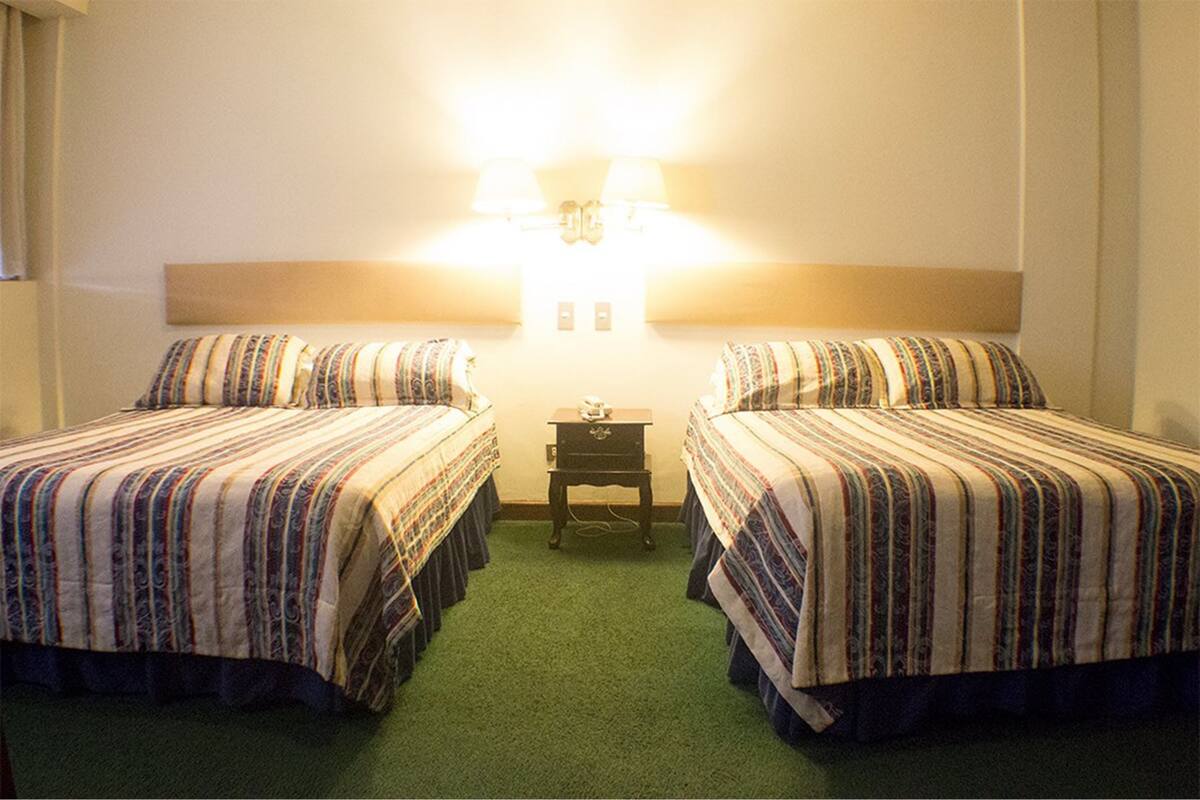 Una habitación de hotel con dos camas, una mesita de noche y una lámpara de pared.
