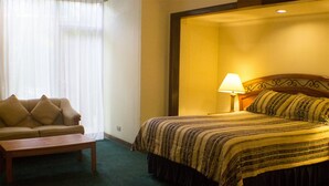 Une chambre d’hôtel avec un lit, un canapé, une lampe et une fenêtre avec des rideaux.