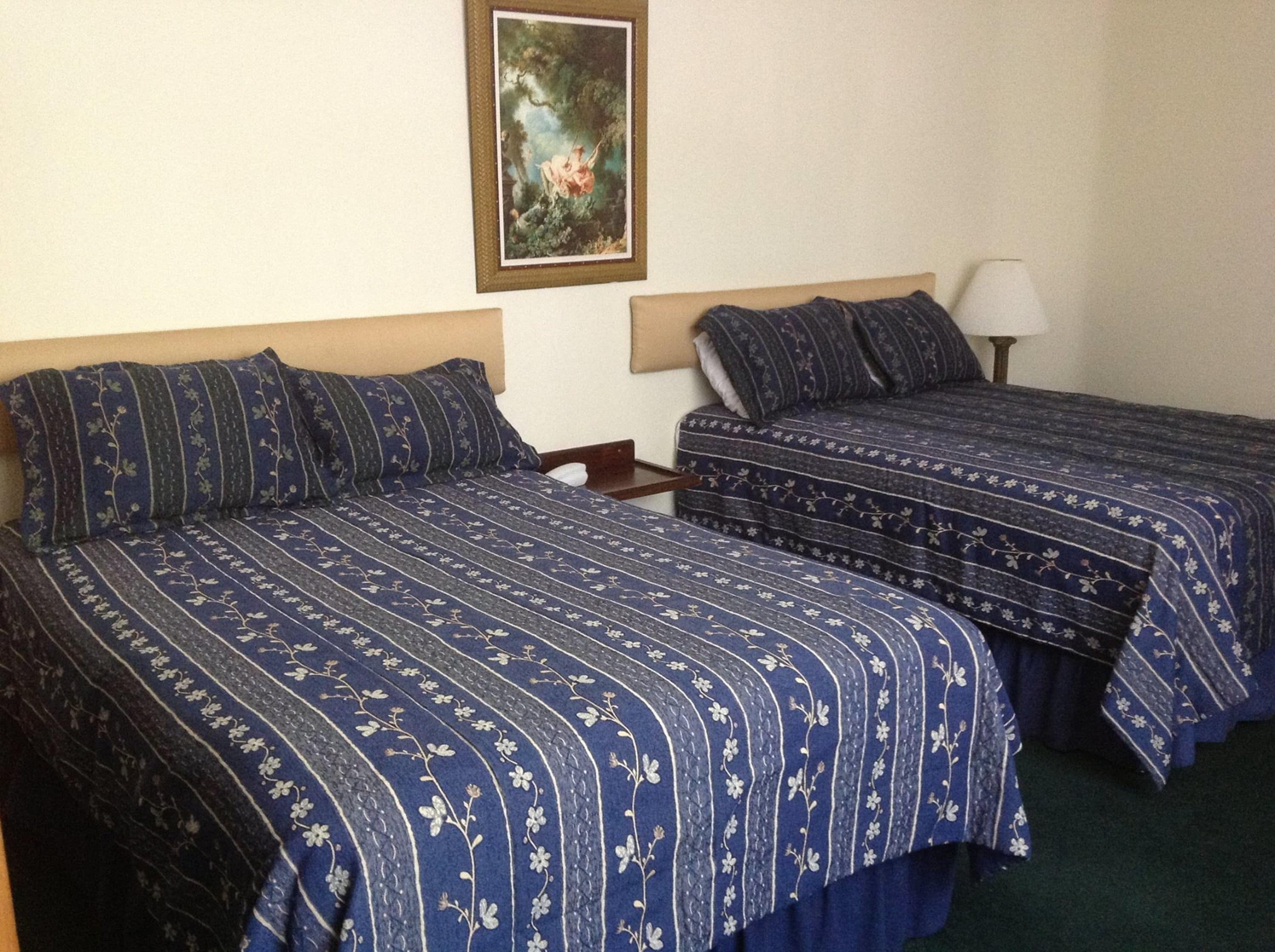 A hotel room with two beds, each with floral-patterned bedding, a nightstand, a lamp, and a framed painting on the wall.