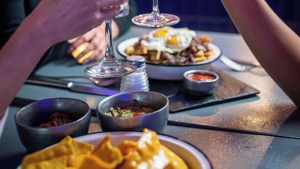 A person holding a cocktail glass with a straw, a glass of iced tea, and a plate of nachos. - Premium Tower Suites (Mendoza)