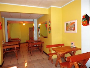 A restaurant interior with wooden tables and benches, yellow walls, and a framed picture on the wall.