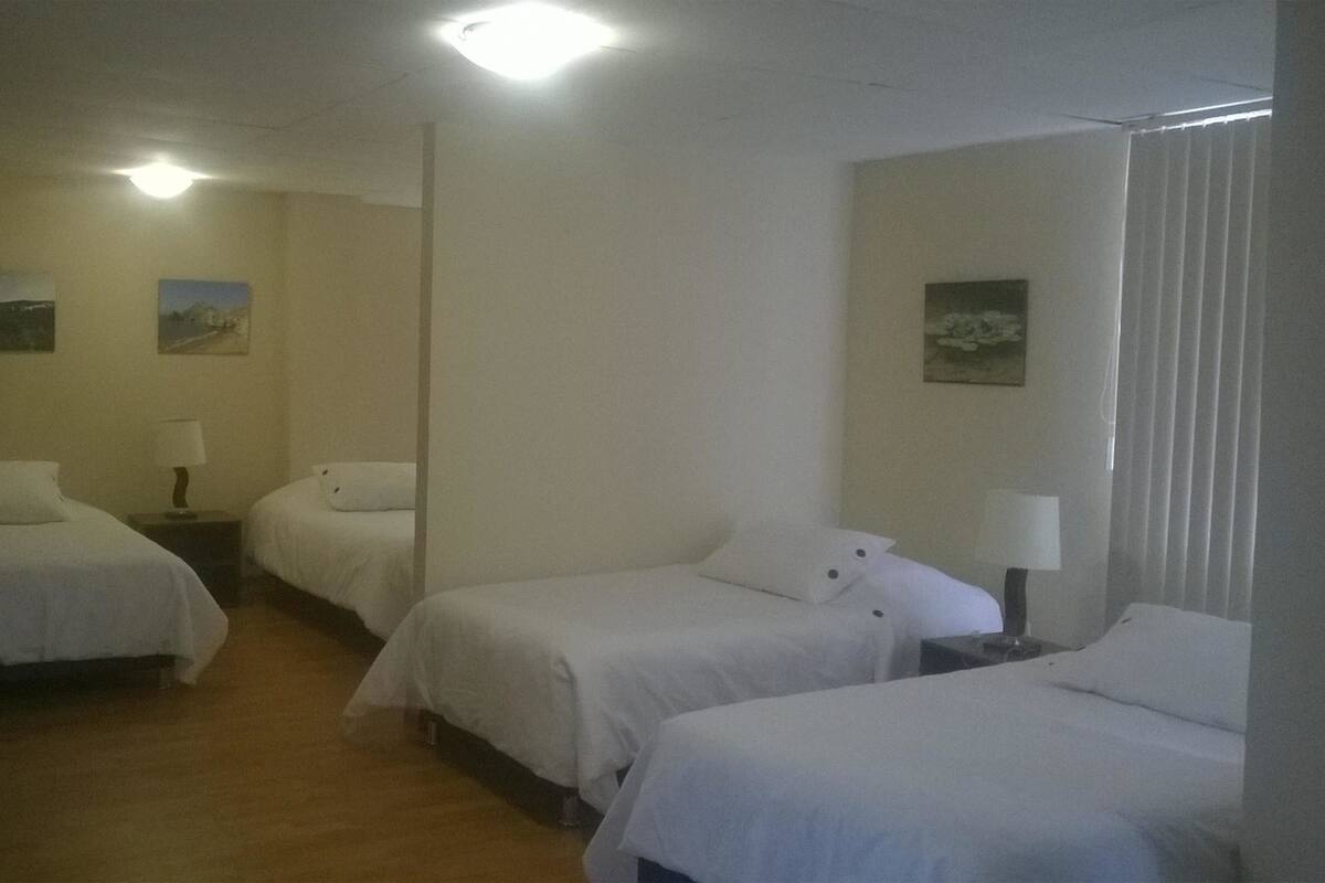 Ein Hotelzimmer mit drei Einzelbetten, Holzboden und zwei Wandlampen.