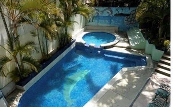 A rectangular swimming pool with a hot tub, surrounded by palm trees and a tiled deck. - Hotel Miramonte & apartments (San Salvador)