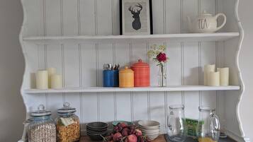 A kitchen with white wooden shelves, jars of grains, a bowl of fruit, and a tea pot.