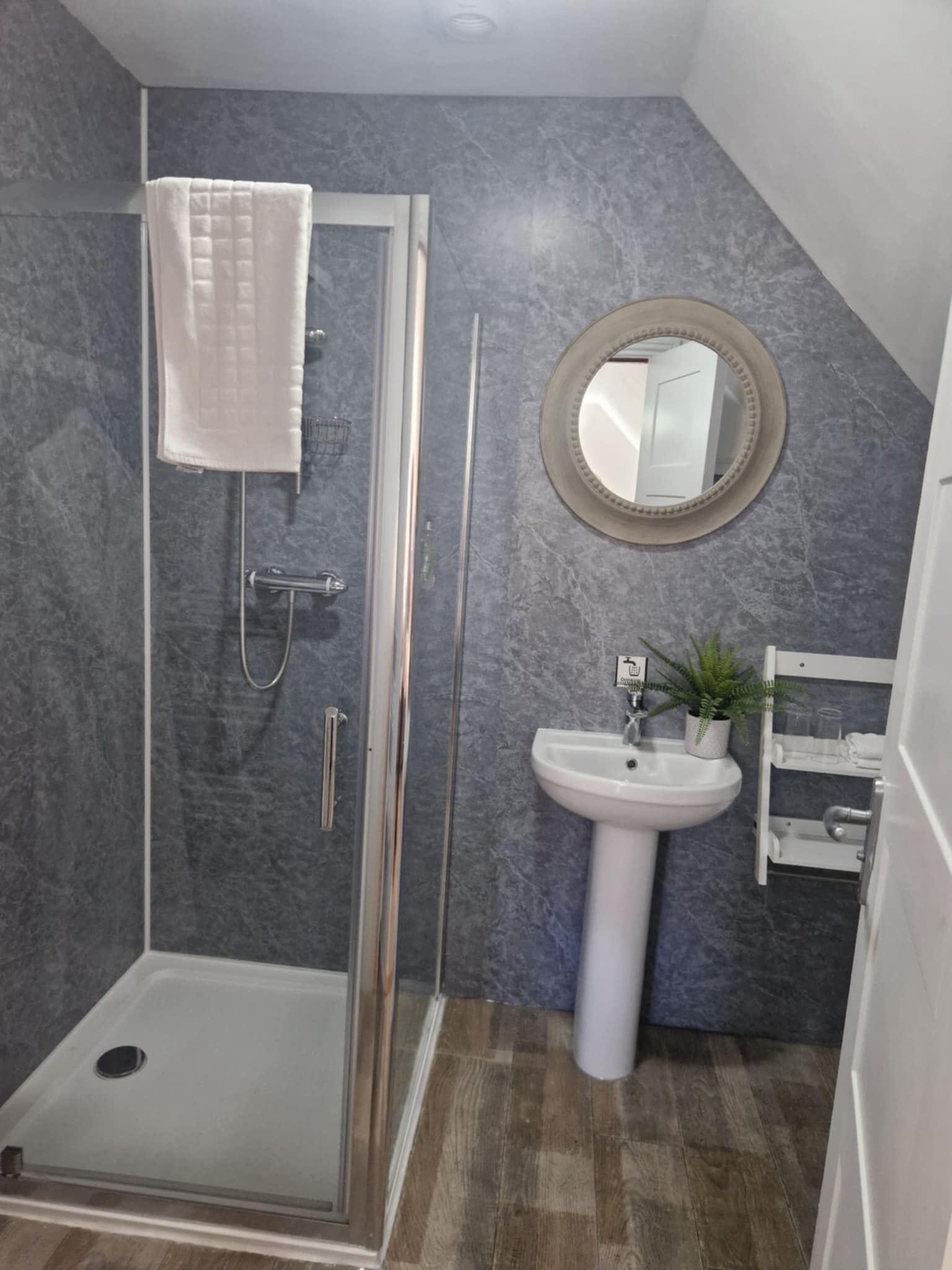 Un bagno con box doccia in vetro, lavandino bianco, specchio e una pianta in vaso.
