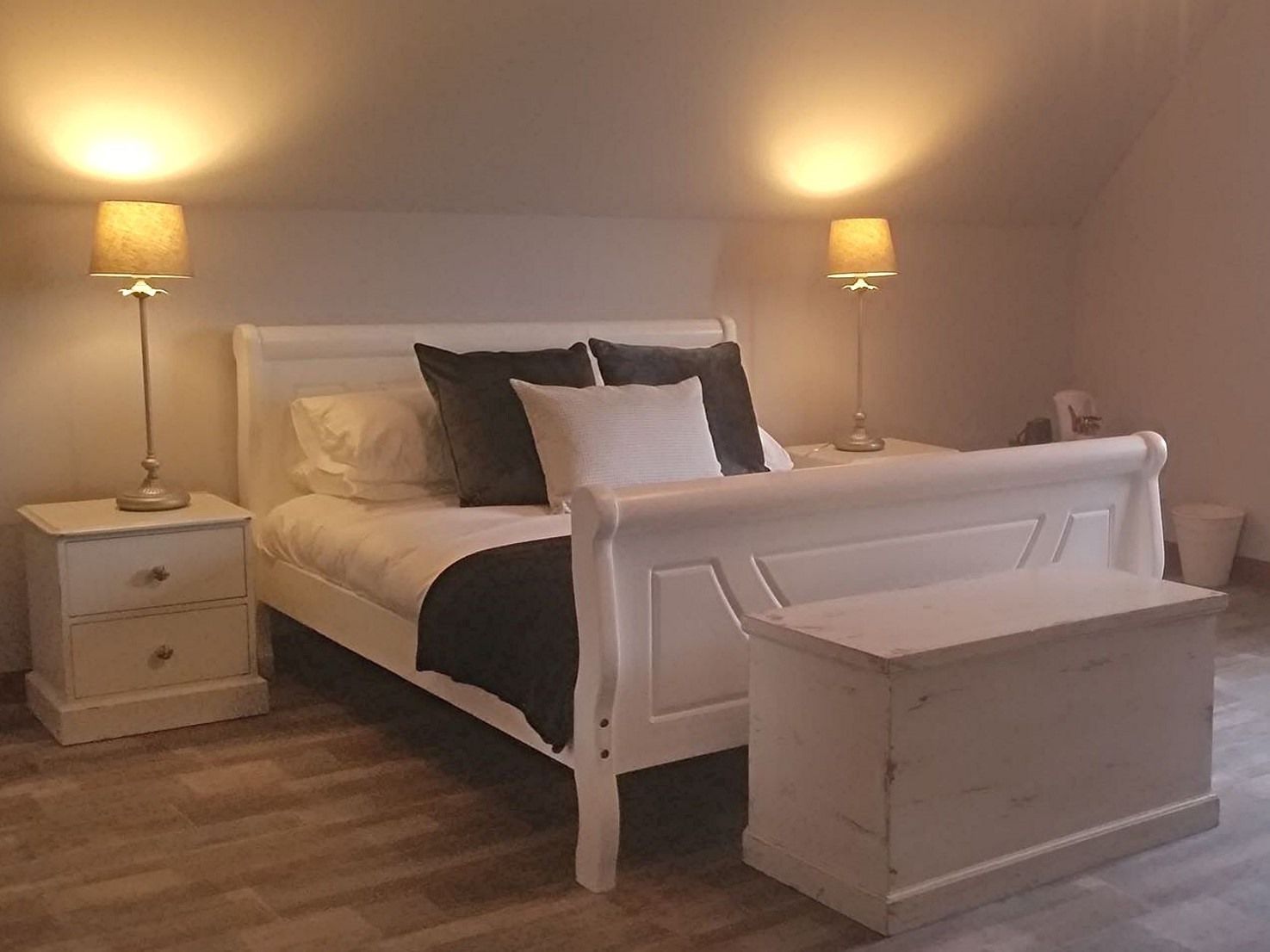 A bedroom with a white bed, two bedside lamps, a nightstand, and a small bedside table.