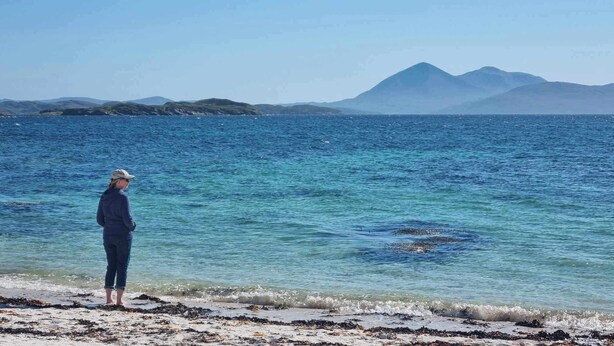A person standing on a beach with clear blue water and distant mountains. - Applecross B&B and Cabins (Strathcarron)