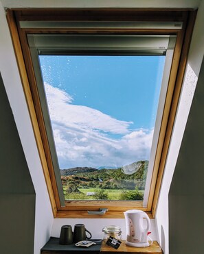 Ein Dachfenster mit Blick auf eine grüne Landschaft und Hügel.