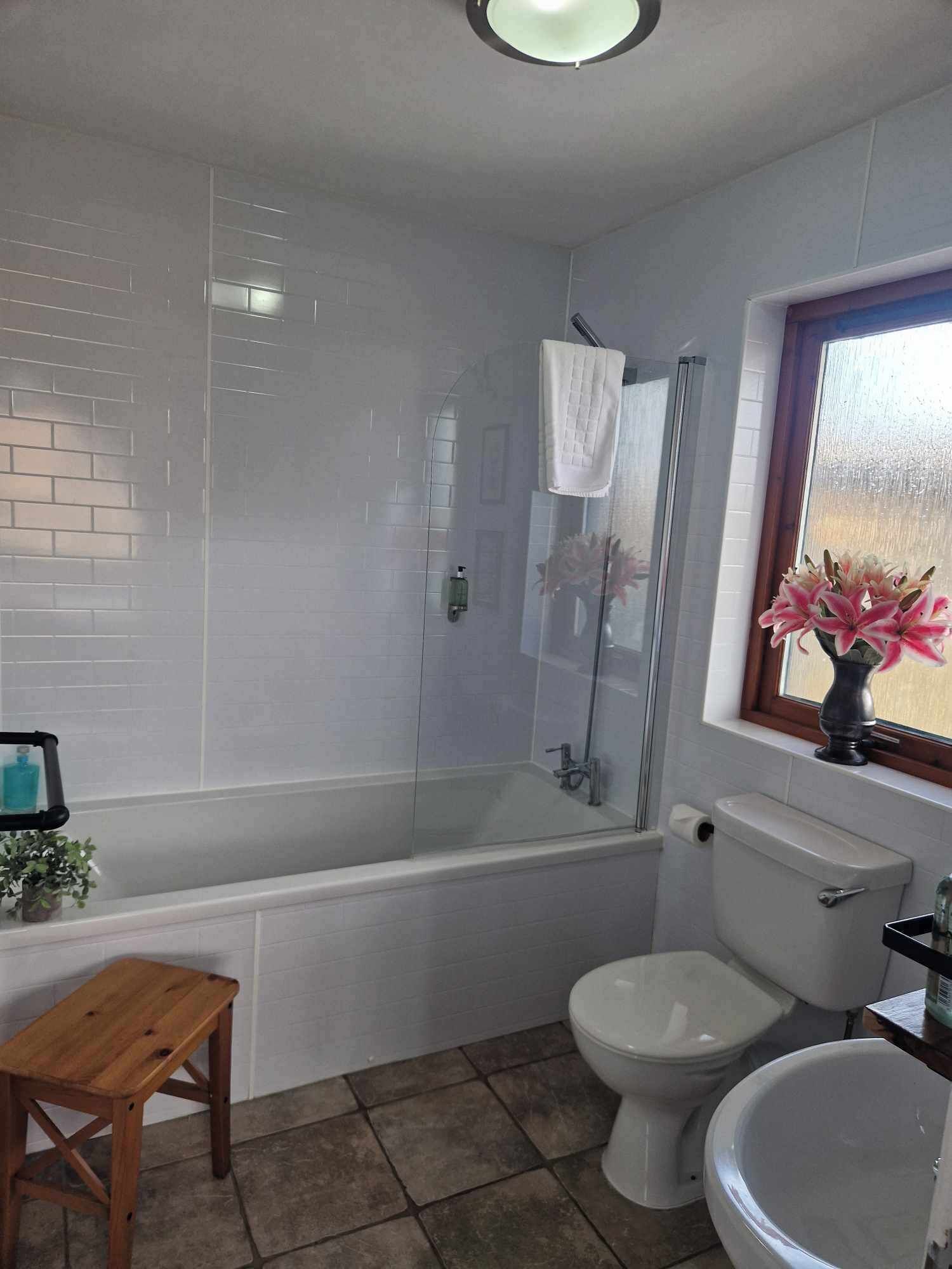 Un baño con bañera, inodoro y un taburete de madera.