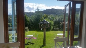 Una habitación con un gran ventanal que da a un jardín con un porche, una mesa y sillas.