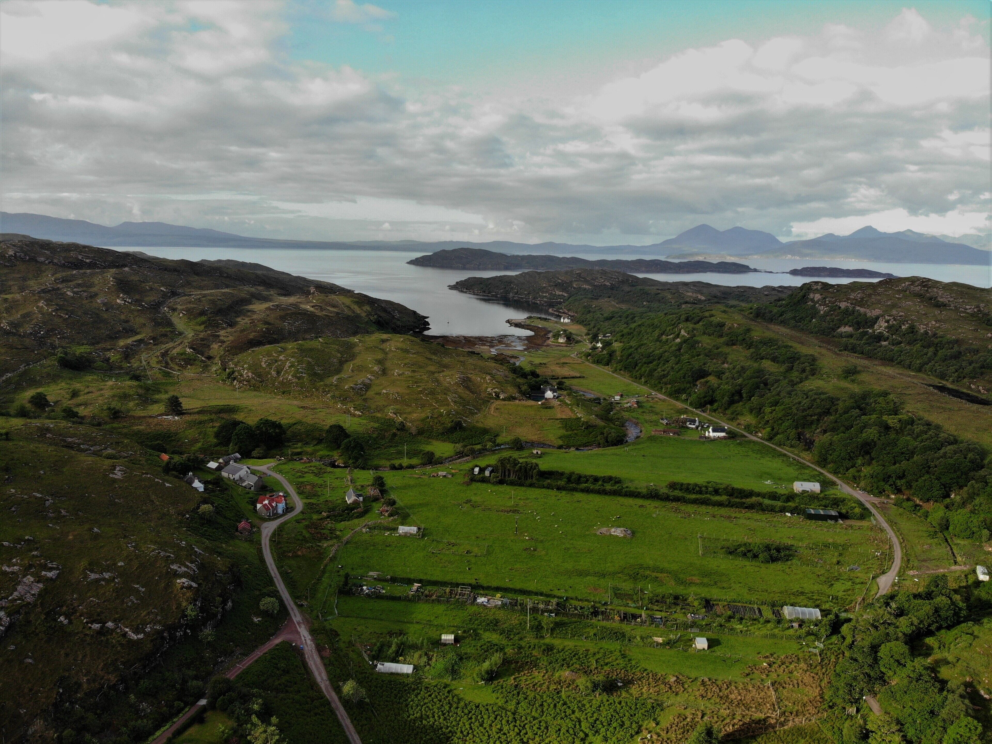 An aerial view of a rural landscape with rolling hills, a winding road, and scattered houses.