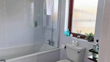 Ein Badezimmer mit Duschkabine, Toilette, Waschbecken und einem hölzernen Hocker.
