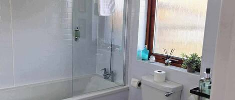 A bathroom with a glass-enclosed shower, a toilet, a sink, and a wooden stool.