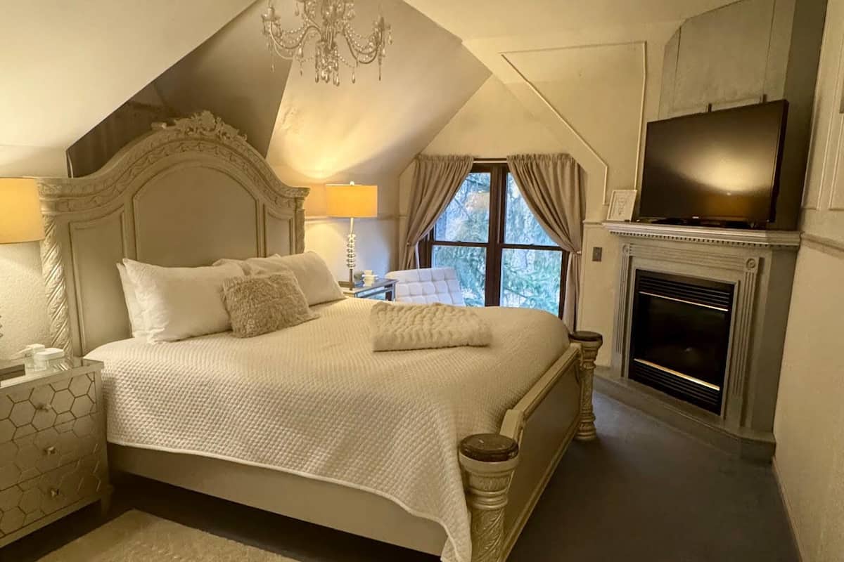 A bedroom with a large bed, a chandelier, a fireplace, and a television.